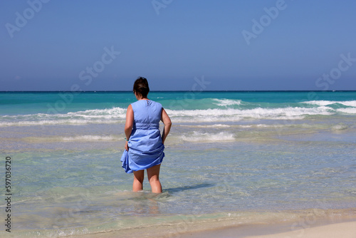 Woman in blue dress going to azure sea water. Travel and beach vacation on sandy coast © Oleg