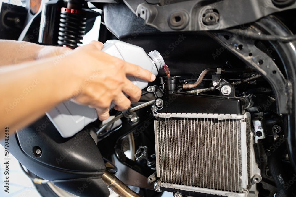 Hands of motorcycle mechanic filling cooling system with engine coolant,pour coolant after
