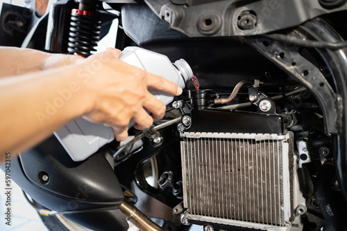 Hands of motorcycle mechanic filling cooling system with engine coolant,pour coolant after repairing or cleaning the radiator,check liquid level in motorcycle radiator,service,maintenance concept photo