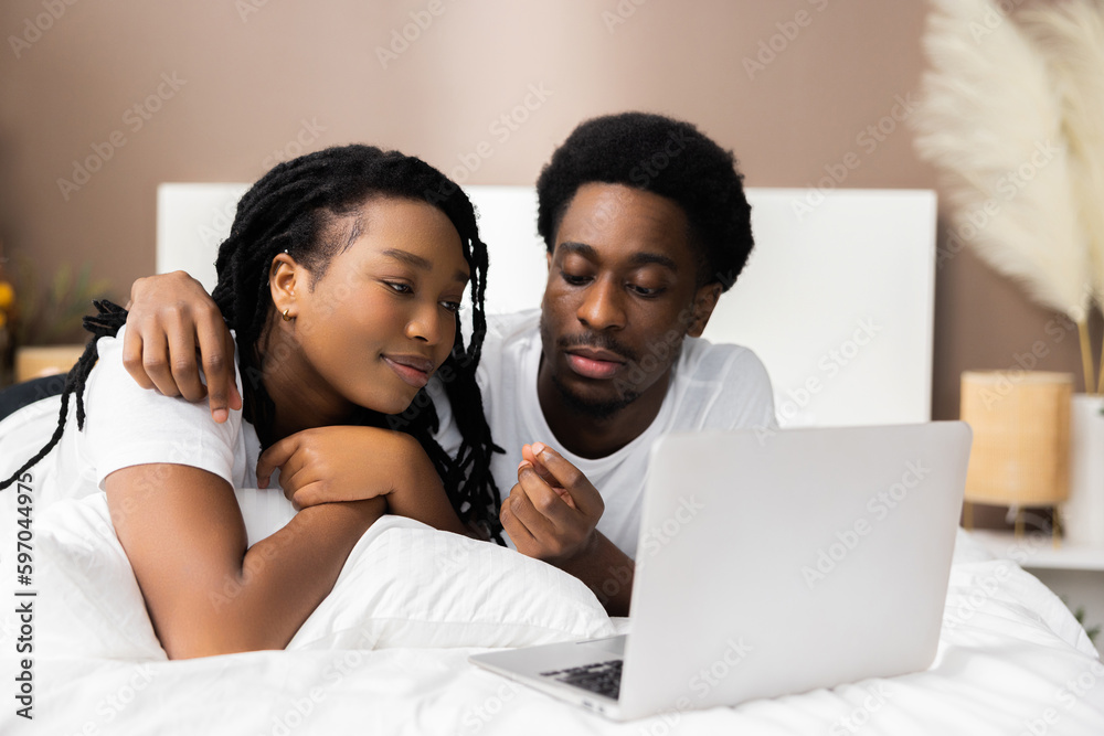 Happy cheerful African American black couple lying on bed in front of ...