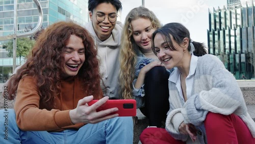 Group of young gen z friends sitting together in the city using cell phone to share funny content photo