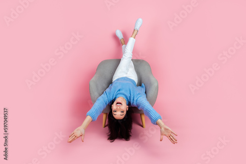 Full size portrait of satisfied girl rejoice sit chair upside down isolated on pink color background
