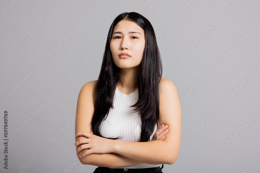 Offensive young cute teenager student girl in studio isolated standing on grey background looking at camera in bad mood angry crossing hands on chest. Offensive young cute teenager student girl in studio isolated standing on grey background looking at camera in bad mood angry crossing hands on chest.
