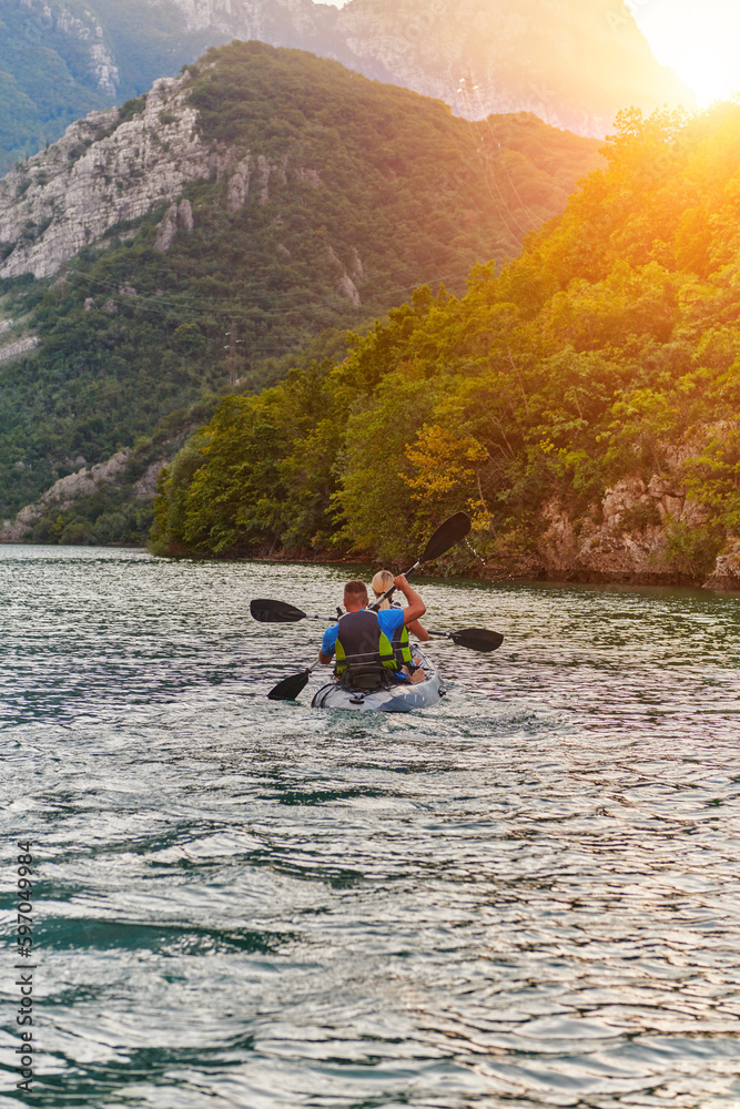 A young couple enjoying an idyllic kayak ride in the middle of a beautiful river surrounded by forest greenery in sunset time 