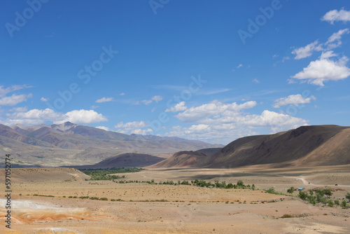 A panoramic view of the valley in the mountains in changeable weather. Shadow over the valley against a blue sky with clouds.