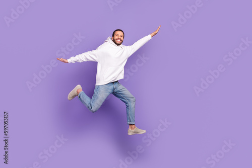 Full body photo of carefree jump flying youngster guy wear white sweatshirt feel lightness just freedom isolated on purple color background