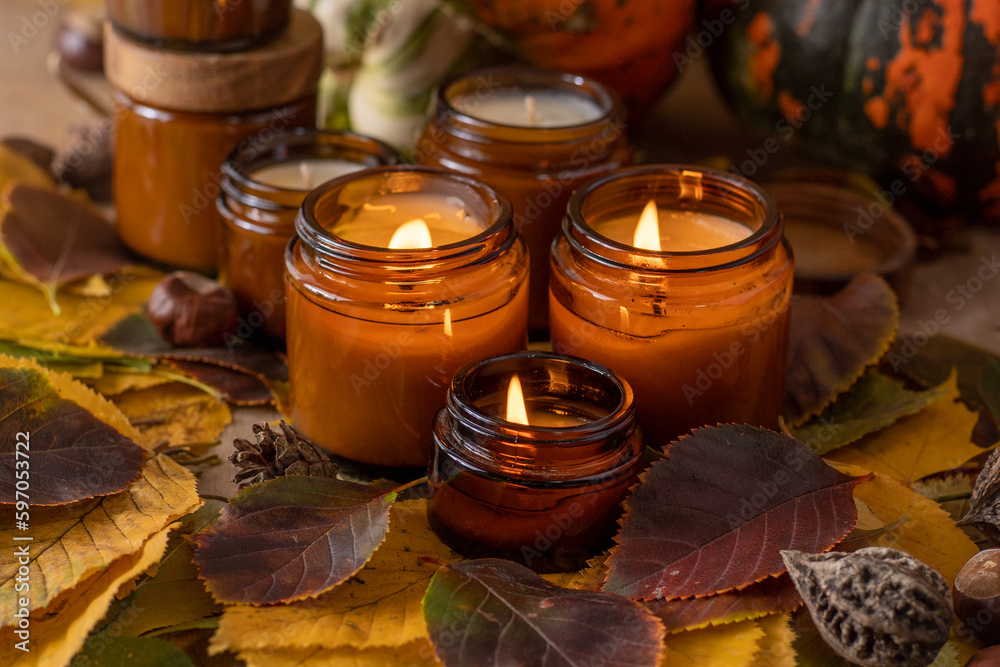Soy candles burn in glass jars. Tree leaves. Comfort at home. Candle in a brown jar. Scent and light. Scented handmade candle. Aroma therapy. Autumn mood. Cozy home decor in fall. Festive decoration.