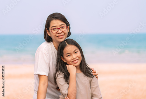 Portrait of Asian mother and small daughter on the beach, soft natural light, middle-aged woman with 9 years old child girl, positive emotion, smiling, single parent, space for copy. © dul_ny