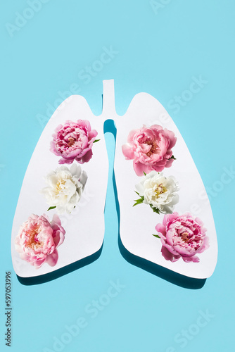 Paper silhouette of anatomical lungs with flowers inside on a blue background. The concept of healthy breathing. Vertical image.