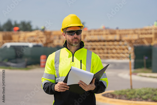 Construction worker at house under construction. Male builder construction worker a job site. Portrait of builder engineer worker in helmet at american house building site background.