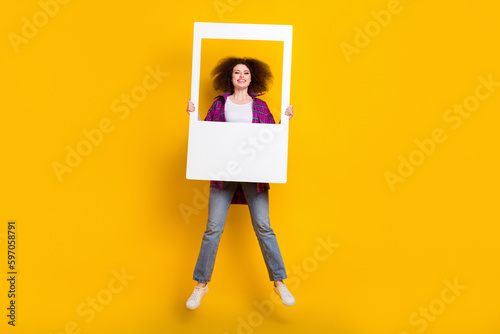 Full length photo of excited shiny woman dressed plaid shirt jumping high taking photo isolated yellow color background