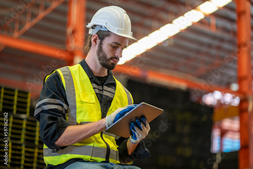 A worker wearing reflective jacket holding digital tablet standing in factory warehouse