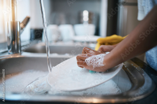 Hands, sink and cleaning dishes with a person in the kitchen of a home to wash a plate for hygiene. Water, bacteria and soap with an adult washing porcelain crockery in a house to clean for housework