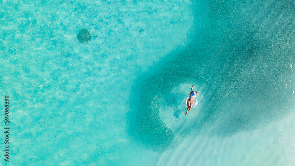 Aerial view with woman in bikini sunbathing as laying on swim ring  as blue sea water in Maldives