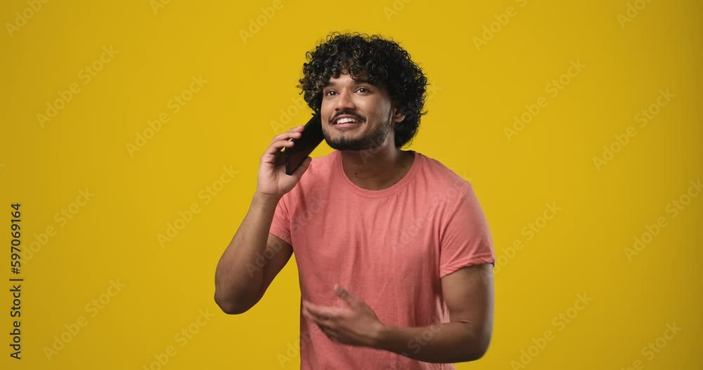 Young smiling indian man talking on the phone answering phone call over yellow orange background