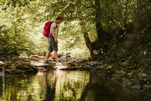 Traveling with backpack concept image. Backpacker female in trekking boots crossing mountain river. Summer vacation trip