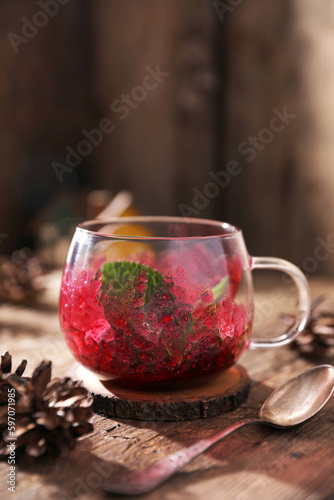 Tea with herbs, berries and fruits in a transparent cup on a wooden background