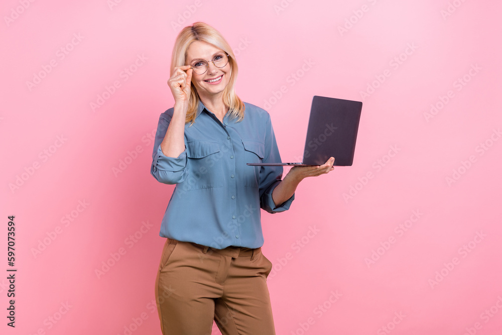 Photo of smiling cheerful business lady wear blue shirt brown pants hold netbook touch glasses director company isolated on pink color background Photo of smiling cheerful business lady wear blue shirt brown pants hold netbook touch glasses director company isolated on pink color background