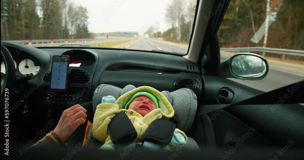 A small child rides in a car seat and cries, mother soothes him by