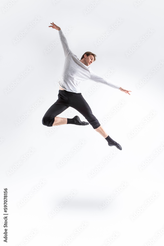 One Professional Caucasian Handsome Young Athlete Man Posing in Flying Ballet Pose with Lifted Hands in White Shirt On White.