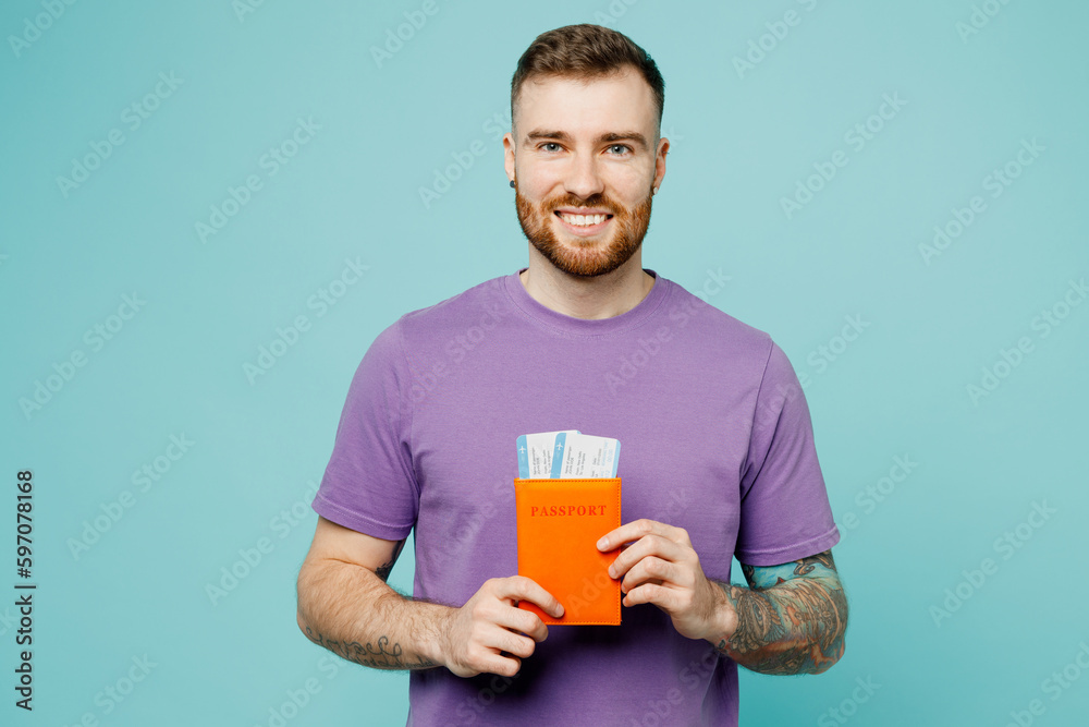 Traveler smiling happy man wear purple t-shirt hold passport ticket isolated on plain pastel blue background. Tourist travel abroad in free spare time rest getaway. Air flight trip journey concept. Traveler smiling happy man wear purple t-shirt hold passport ticket isolated on plain pastel blue background. Tourist travel abroad in free spare time rest getaway. Air flight trip journey concept.