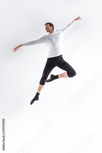 Professional Caucasian Handsome Young Athlete Man Posing in Flying Ballet Pose with Lifted Hands in White Shirt On White.