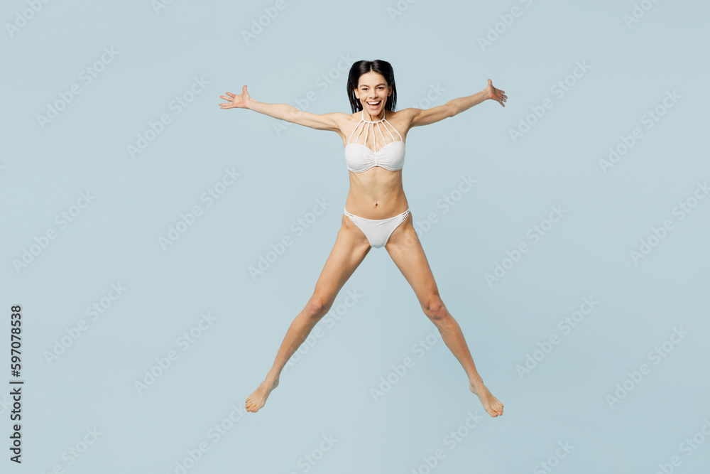 Full body young sexy woman wears swimsuit jump high with outstretched hands arms look camera near hotel pool isolated on plain pastel light blue background. Summer vacation sea rest sun tan concept.