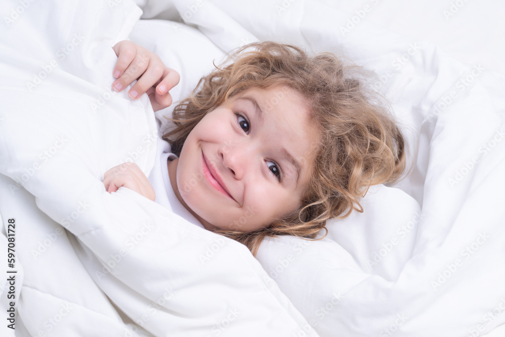 Child enjoys sunny morning. Good time at home. Kid wakes up from sleep. Child wakes up in morning in bed. Morning awakening little child in bed.