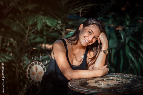 beautiful young Latina woman sitting at a table with jungle type background photo