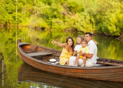 Happy family of four sitting in a boat on the lake and looking away