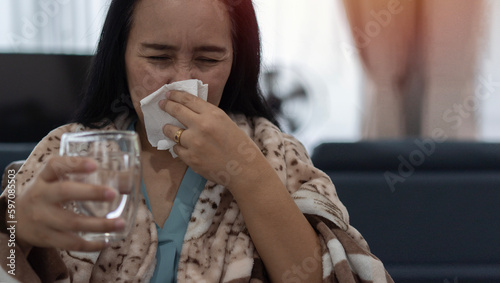 Asian female blowing nose, coughing or sneezing in tissue at home, suffering from flu.