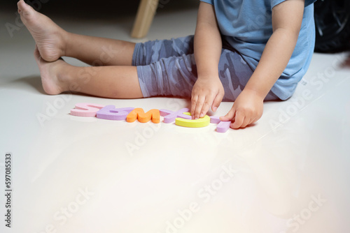 Clopped image of little toddler boy playing with colorfull alphabets collection on the floor.