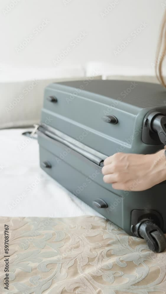 The young woman packs her things on the bed in a suitcase. Sunny day. Closes the suitcase Vertical video. The young woman packs her things on the bed in a suitcase. Sunny day. Closes the suitcase Vertical video.