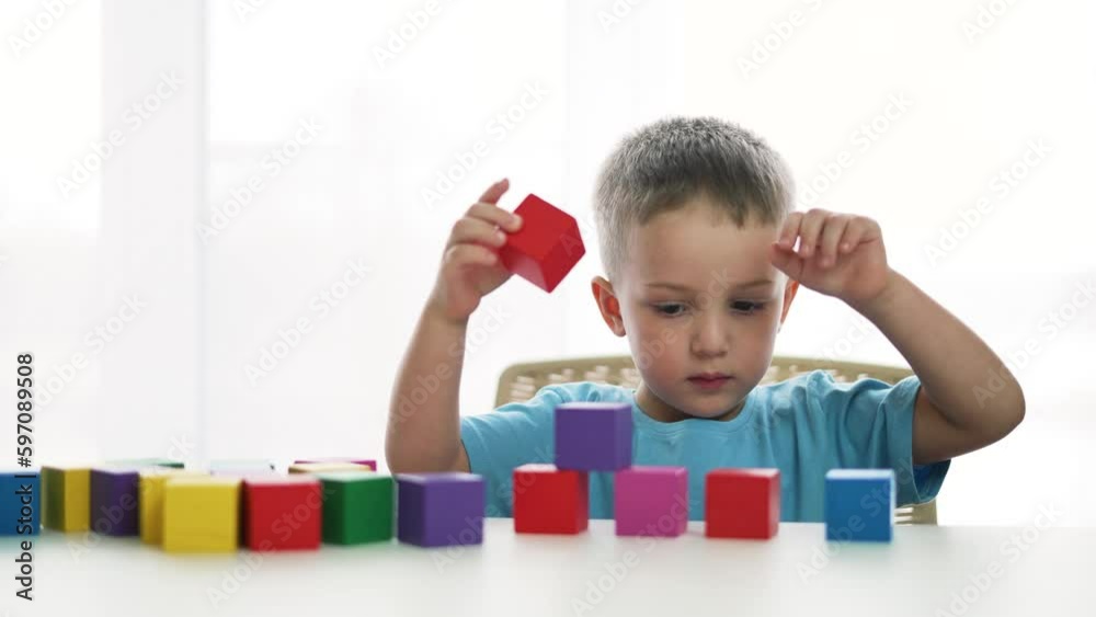 Adorable children play in kindergarten and at home. Colored cubes and toys on table. Child collects toys in kindergarten. Child home game. Concept of family happy.Kid with colored cubes plays at table Adorable children play in kindergarten and at home. Colored cubes and toys on table. Child collects toys in kindergarten. Child home game. Concept of family happy.Kid with colored cubes plays at table