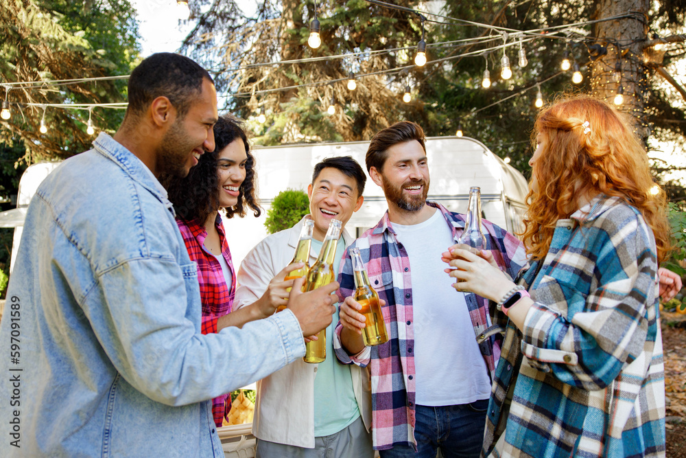 A cheerful multinational company is having fun on a picnic. Multisex friends sitting at the table outdoors celebrating eating and drinking drinks. A cheerful multinational company is having fun on a picnic. Multisex friends sitting at the table outdoors celebrating eating and drinking drinks.