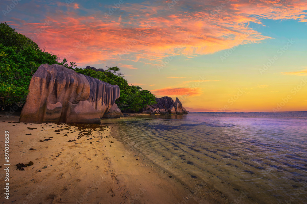 Colorful sunset over Anse Source D'argent beach at the La Digue Island, Seychelles, with calm water of the Indian Ocean and amazing granite rock formations.