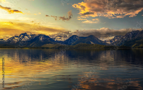 Summer sunset above Lake Tahoe with snowy Sierra Nevada Mountains and beautiful reflection in the water.