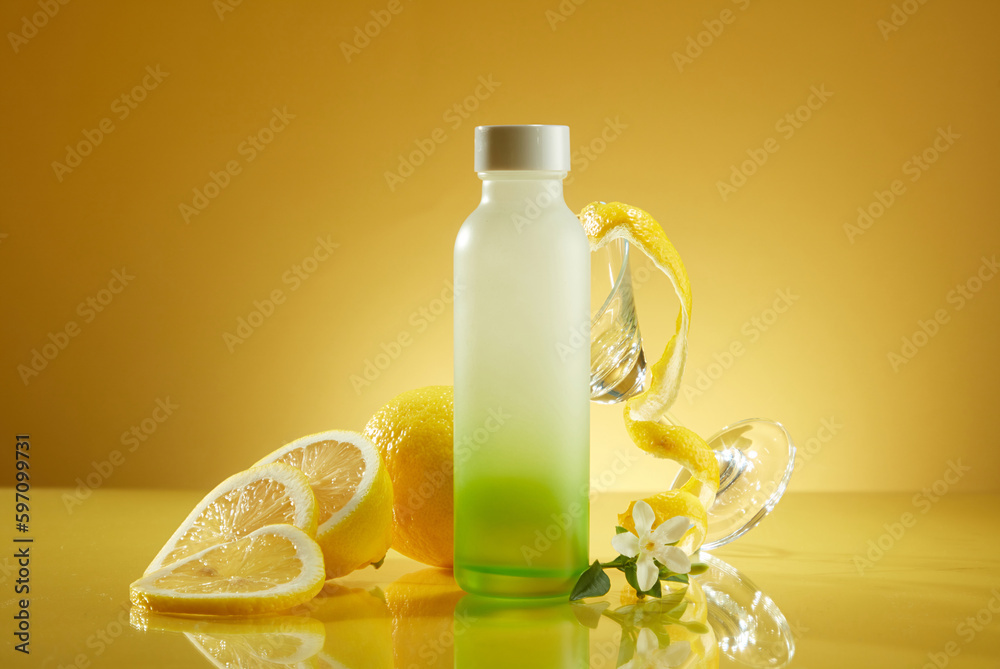 Front view glass bottle unbranded with fresh lemon and glass cup on yellow background. Packaging for beverage products with fresh lemon flavor for a refreshing feeling Front view glass bottle unbranded with fresh lemon and glass cup on yellow background. Packaging for beverage products with fresh lemon flavor for a refreshing feeling