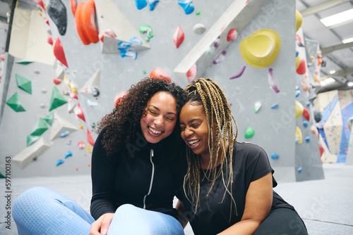 Two Smiling Female Friends Having Fun Laughing As They Try Climbing Wall At Indoor Activity Centre photo