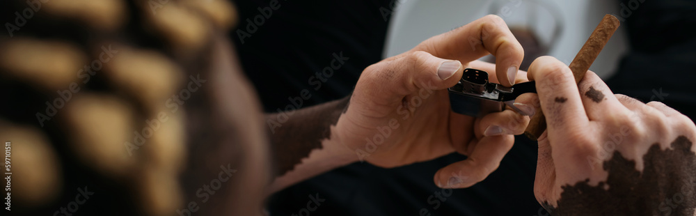 Cropped view of african american man with vitiligo holding lighter and cigar in bathtub, banner. Cropped view of african american man with vitiligo holding lighter and cigar in bathtub, banner.