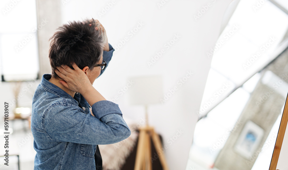 Fototapeta premium Mature woman adjusts her short haircut near the mirror.