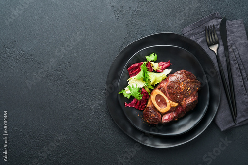 Steaks Osso Buco. Sliced beef grilled Osso Buco or porterhouse meat steak with garnished with salad and french fries on black marble board on old wooden background. Top view. Mock up.