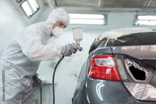 Automotive paint services, quality auto body shop concept. Male car mechanic working with spray gun painting on auto body in automotive paint service shop. Automobile painter painting car in chamber