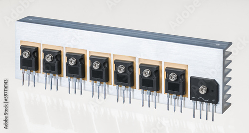 Electrical components on aluminum heat sink of switch-mode power supply on white background. Set of insulated gate bipolar transistors on silicone washers and bridge rectifier screwed on metal cooler. photo