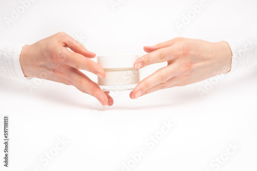 Mock-up of beautiful woman's hand holds round jar or container of cosmetic product cream or lotion on white isolated background. Concept of beauty, spa industry, skin care. Close-up, copy space © artemidovna