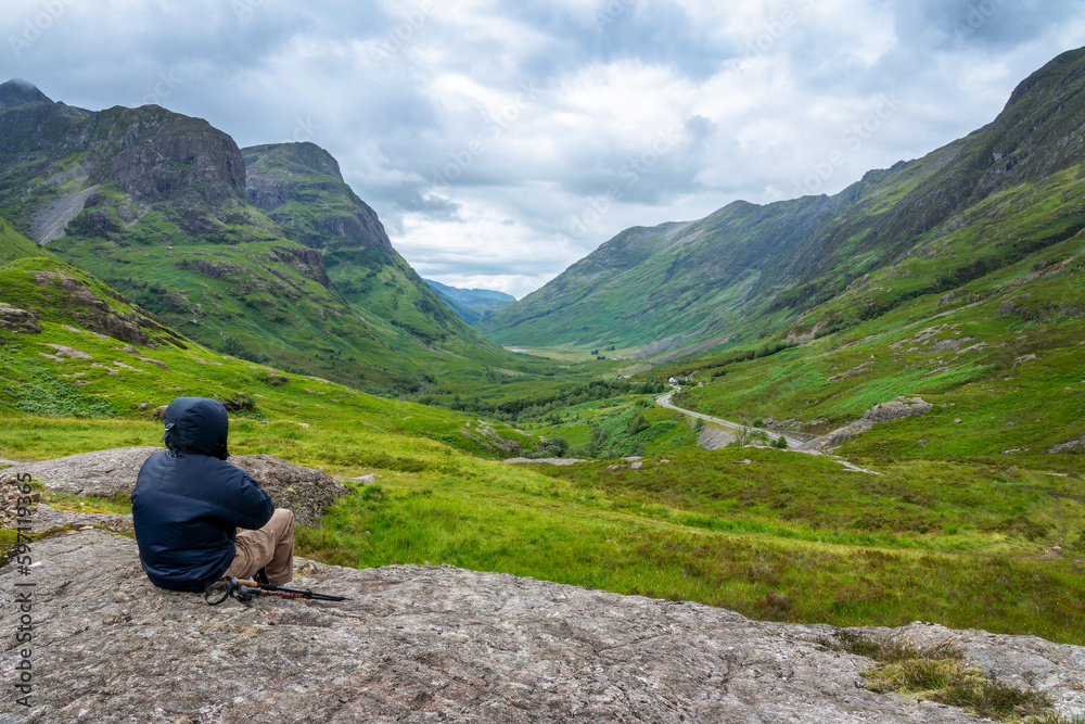 Fototapeta premium Unrecognizable hiker looking at Glencoe valley in summer, Highlands of Scotland, UK
