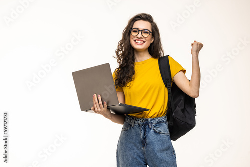 Smiling female student with win gesture holding laptop and looking at camera isolated on a white background