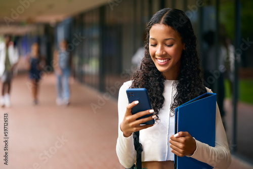 Female Secondary Or High School Student Outdoors At School Going To Class Looking At Mobile Phone