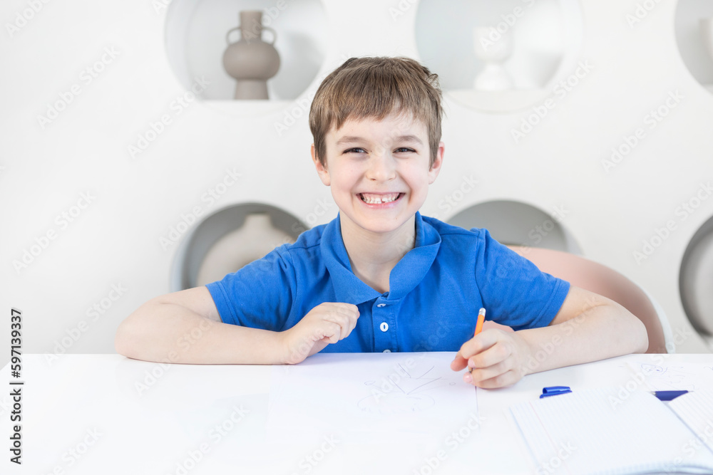 Cute and happy school boy sits at the desk and learns his lessons Cute and happy school boy sits at the desk and learns his lessons