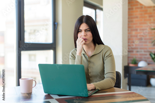 pretty young woman feeling scared, worried or angry and looking to the side. laptop and desk concept